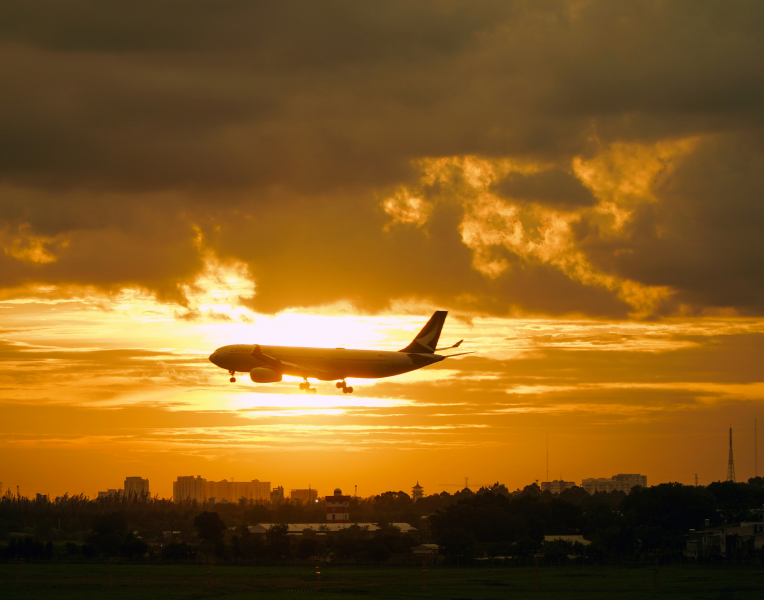 Passenger airplane landing at sunset over a city skyline, golden clouds above the airport.