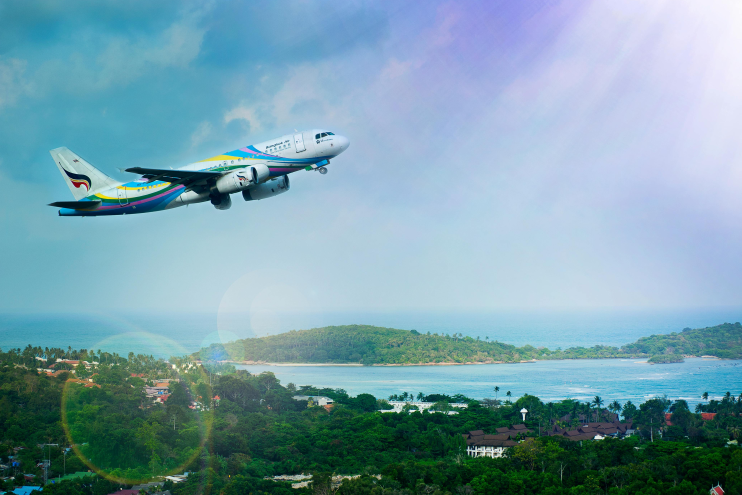 Passenger airplane taking off over a tropical coastline with blue sea and islands in sunlight.
