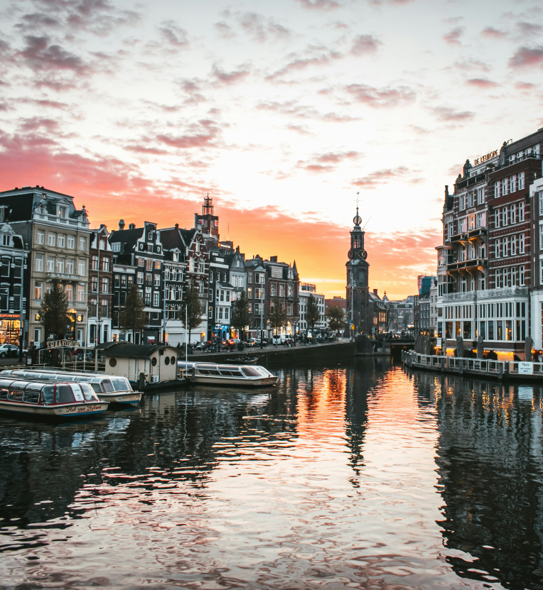 Hotels Near Amsterdam Schiphol (AMS). Sunset over Amsterdam canal with tour boats and the historic Munttoren tower in the background