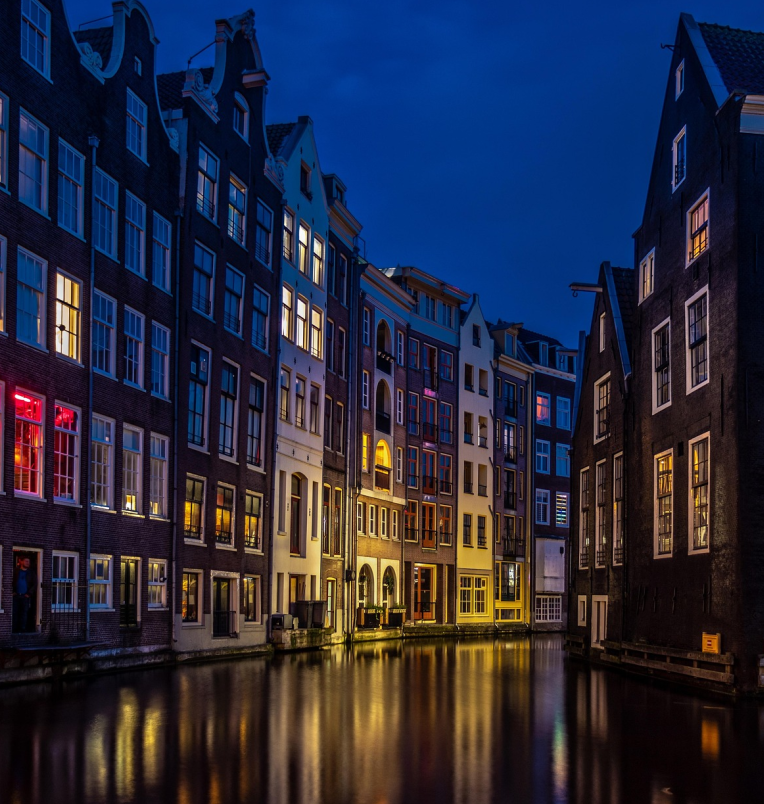 Amsterdam canal houses glowing at night with colourful lights reflecting on the water in the Red Light District.