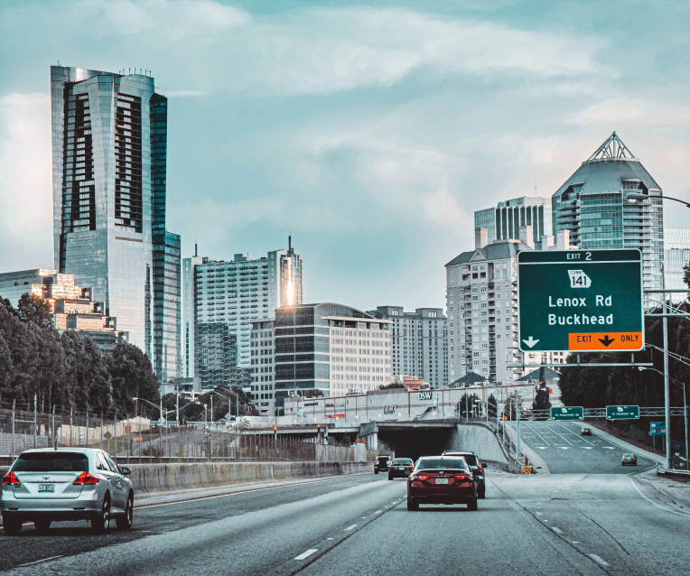 Buckhead Atlanta skyline viewed from the highway with cars and a Lenox Road exit sign.