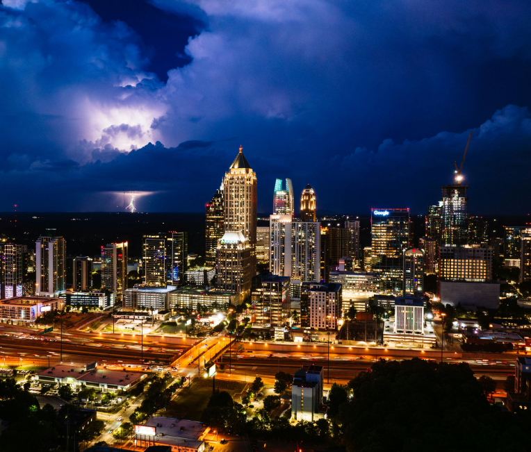 Midtown Atlanta skyline at night with a thunderstorm and lightning in the distance.