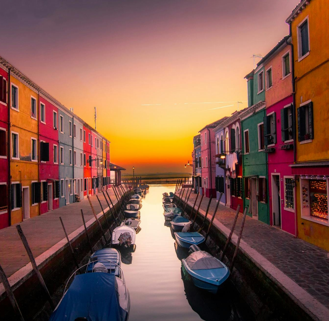 Where2Stay: Find the Best Hotels Near City Hotspots & Airports Worldwide. Colourful houses and boats on a canal at sunset in Burano, Venice, Italy.