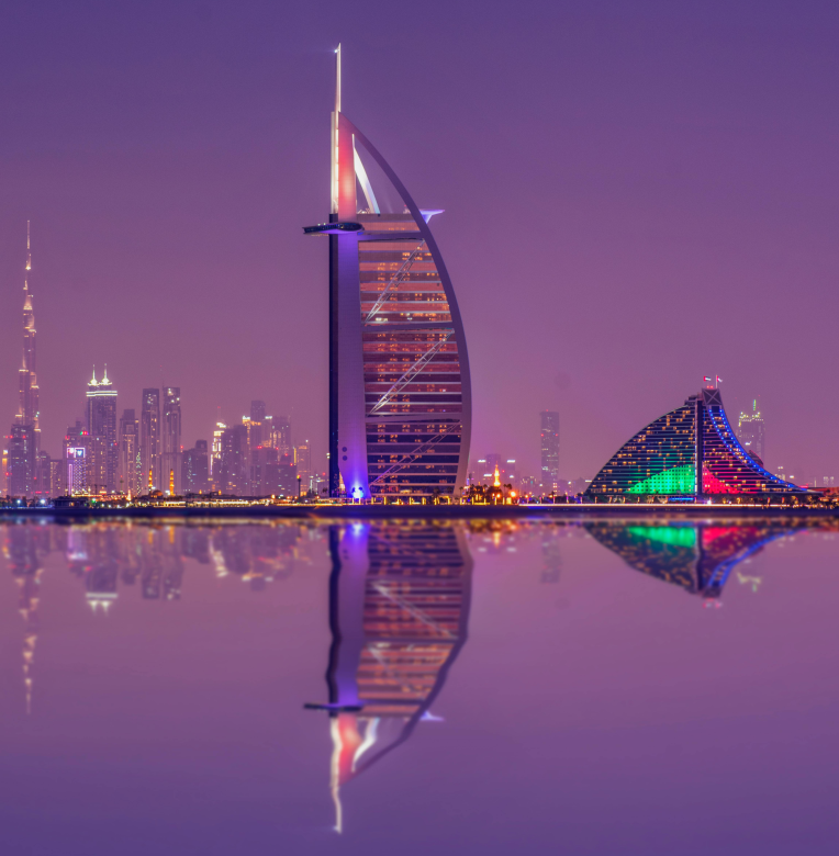 Hotels Near Dubai International Airport (DXB). Burj Al Arab with the Dubai skyline at dusk, reflected on calm water near Jumeirah.