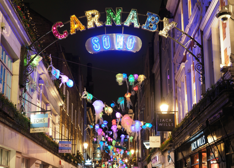 Carnaby Street in Soho, London, lit with colourful neon arch and festive hanging lights at night.