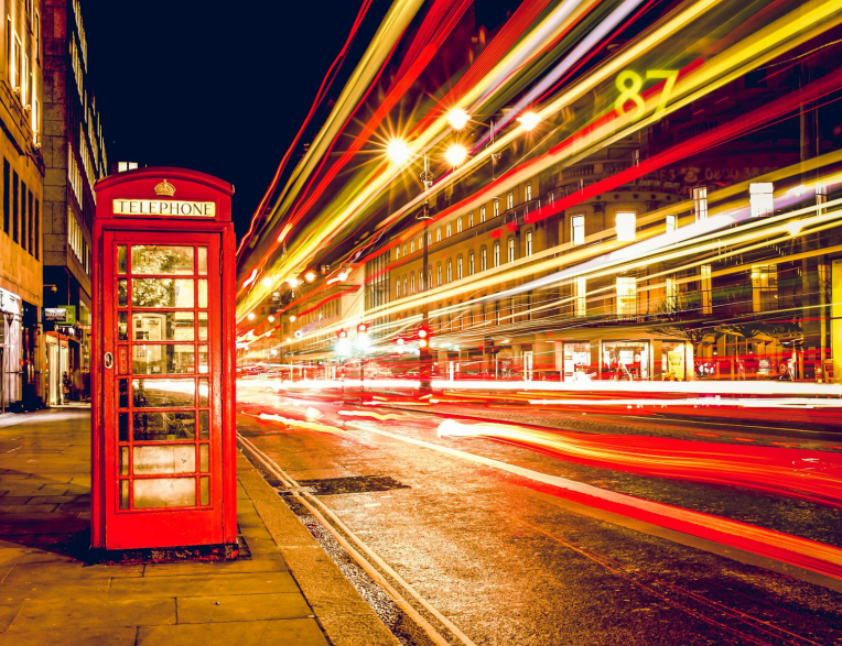 Red telephone box on a Central London street at night with light trails from passing traffic.