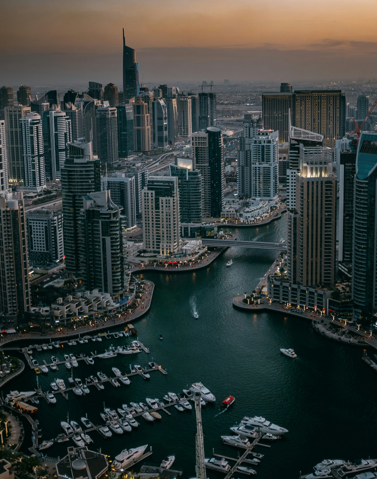 Dubai Marina skyline at sunset with waterfront hotels, high-rise buildings, and moored yachts