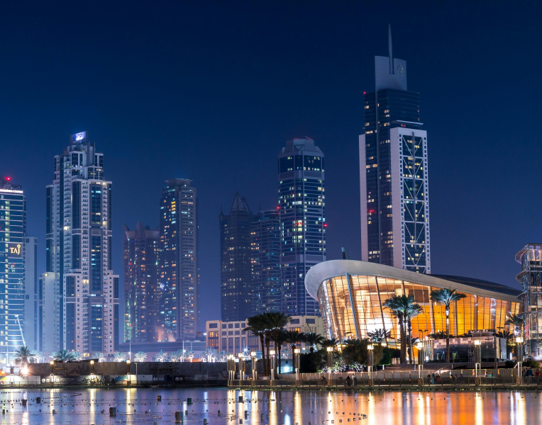 Dubai Opera illuminated at night in Downtown Dubai with skyscrapers reflected on Burj Lake.