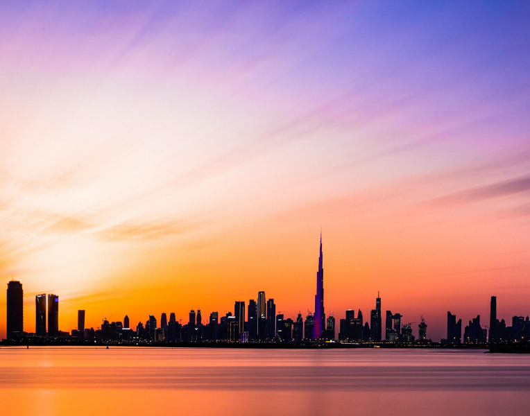 Dubai skyline with the Burj Khalifa at sunset, reflected over calm waterfront.