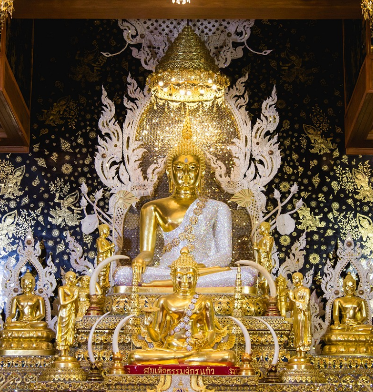Golden Buddha statue surrounded by intricate gold decorations and ornate temple artwork inside a traditional Thai shrine.