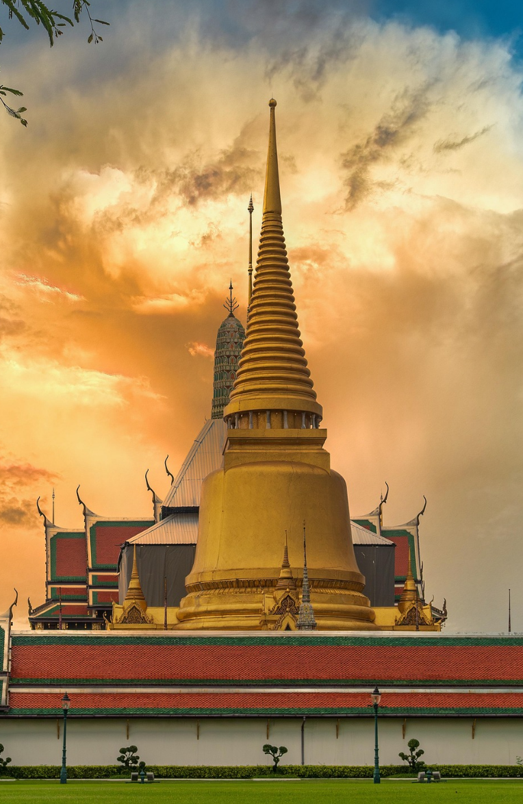Golden stupa at the Grand Palace in Bangkok glowing against a dramatic sunset sky, showcasing traditional Thai temple architecture.