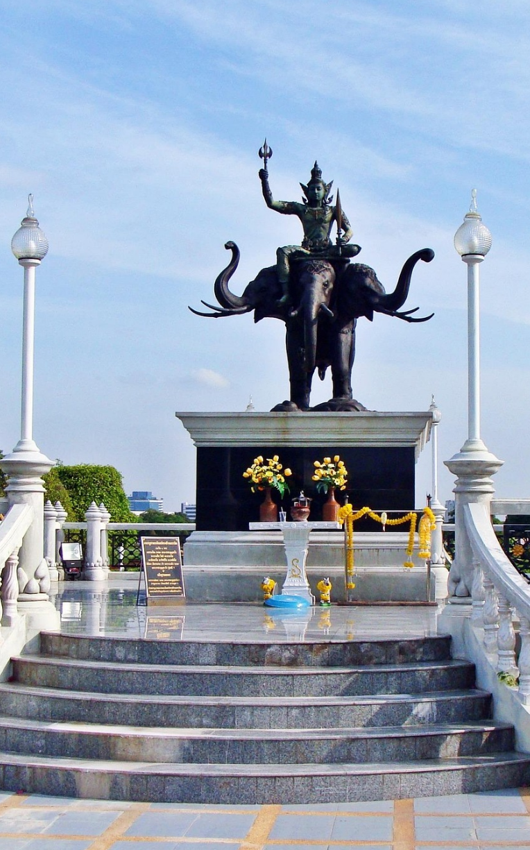 Statue of the Hindu god Indra riding the three-headed Erawan elephant, displayed on a raised marble platform at a monument site in Bangkok, Thailand.
