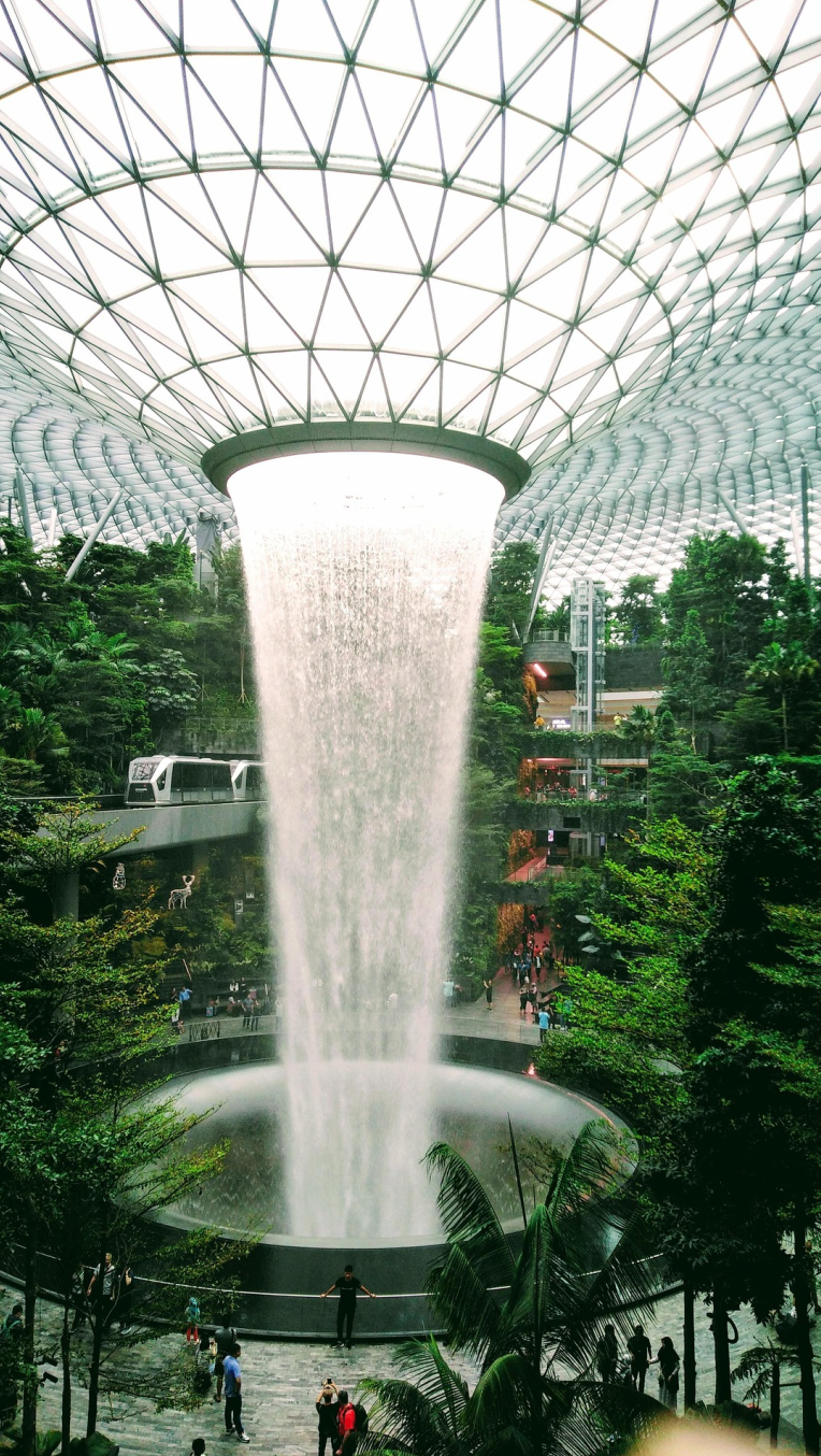 Hotels Near Singapore Changi Airport (SIN). Jewel Changi Airport Rain Vortex waterfall surrounded by indoor forest and glass dome architecture in Singapore.