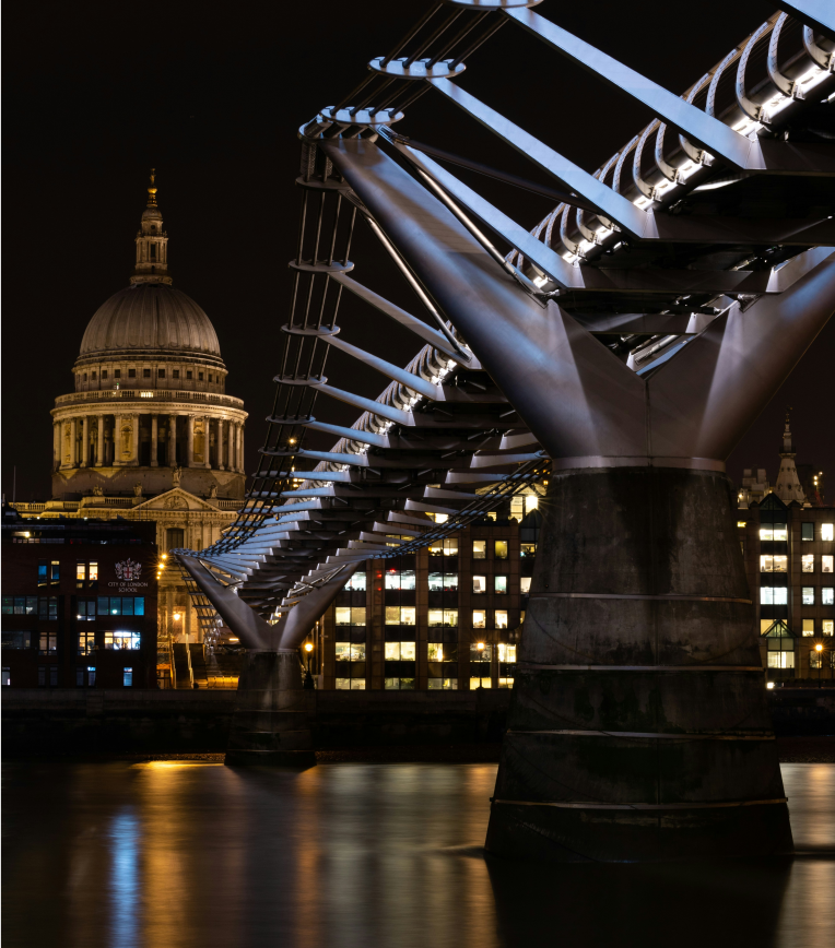 Millennium Bridge at night over the River Thames with St Paul’s Cathedral dome illuminated in the background, London, UK.