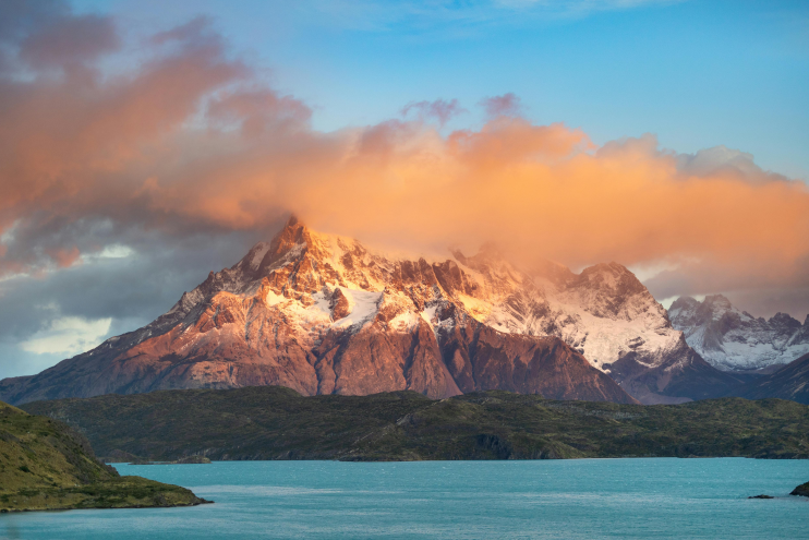 Sunrise over snow-capped Patagonia mountains in Torres del Paine with a turquoise lake in the foreground.