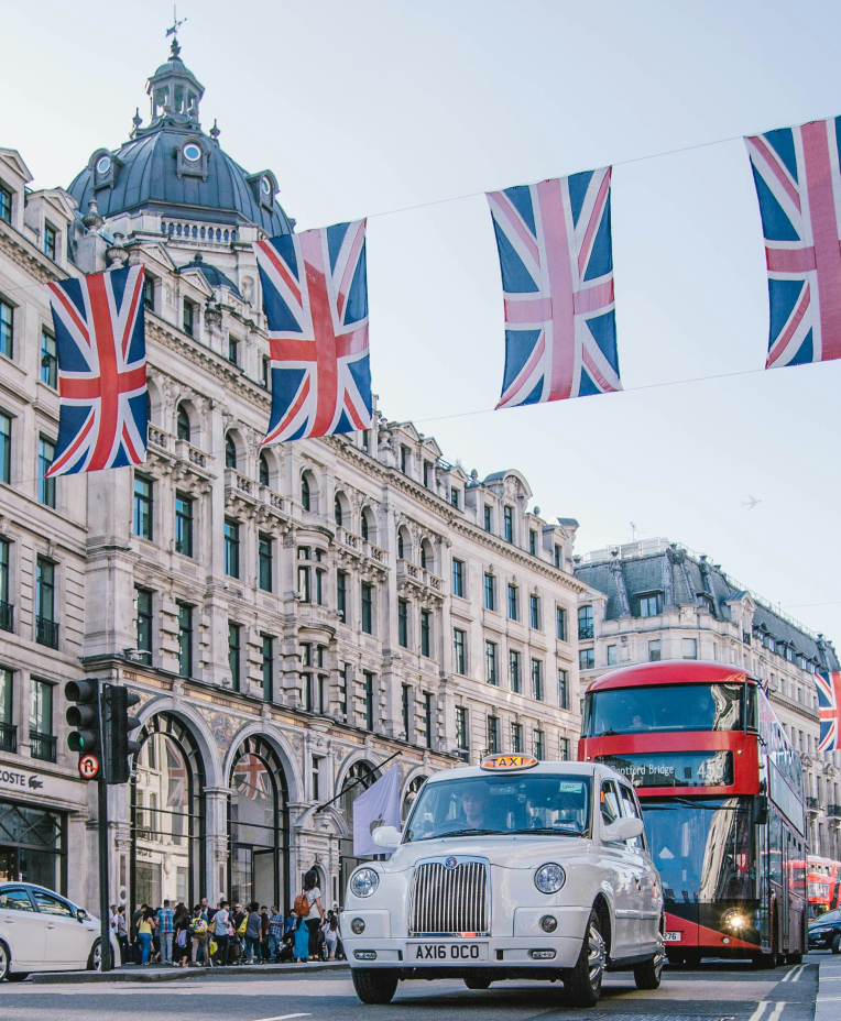 Regent Street scene in London with Union Jack bunting, a white cab, and a red double-decker bus.