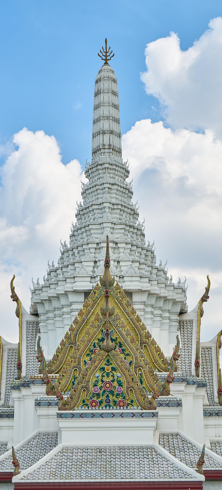 Where to Stay in Bangkok, Thailand. Ornate white prang with a colourful, intricately decorated gabled roof at a traditional Thai temple under a blue sky.