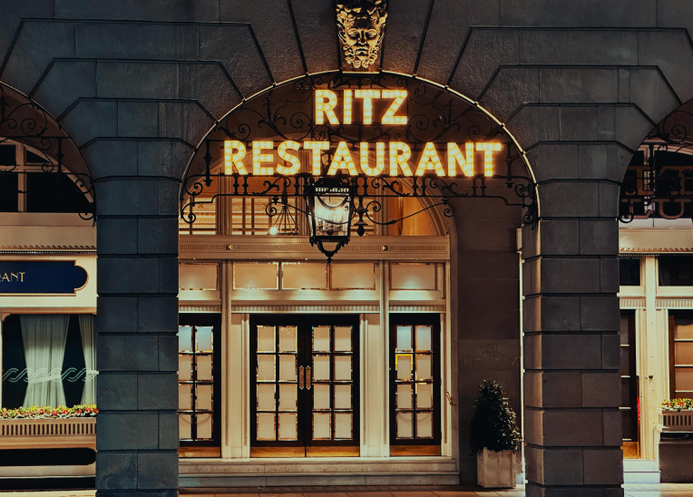 Elegant arched doorway of The Ritz Restaurant, Piccadilly, London, glowing marquee at night.