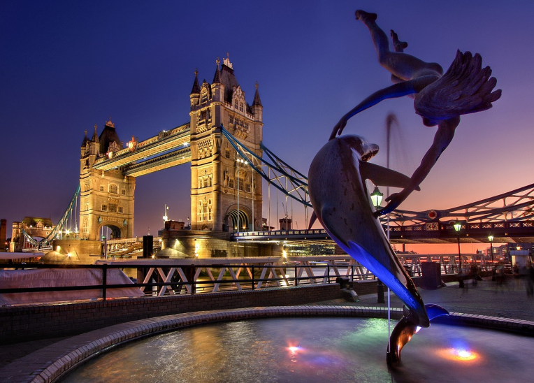 Tower Bridge at sunset with the ‘Girl with a Dolphin’ fountain in the foreground on the River Thames, London, UK.