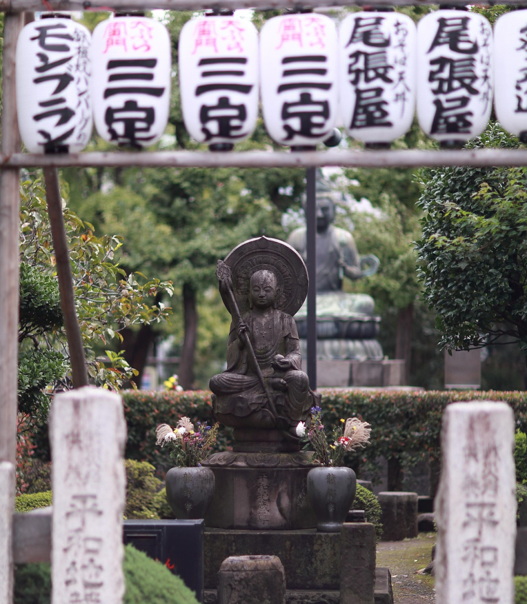 Stone Buddha statue in a peaceful Japanese temple garden in Tokyo with traditional lanterns overhead.