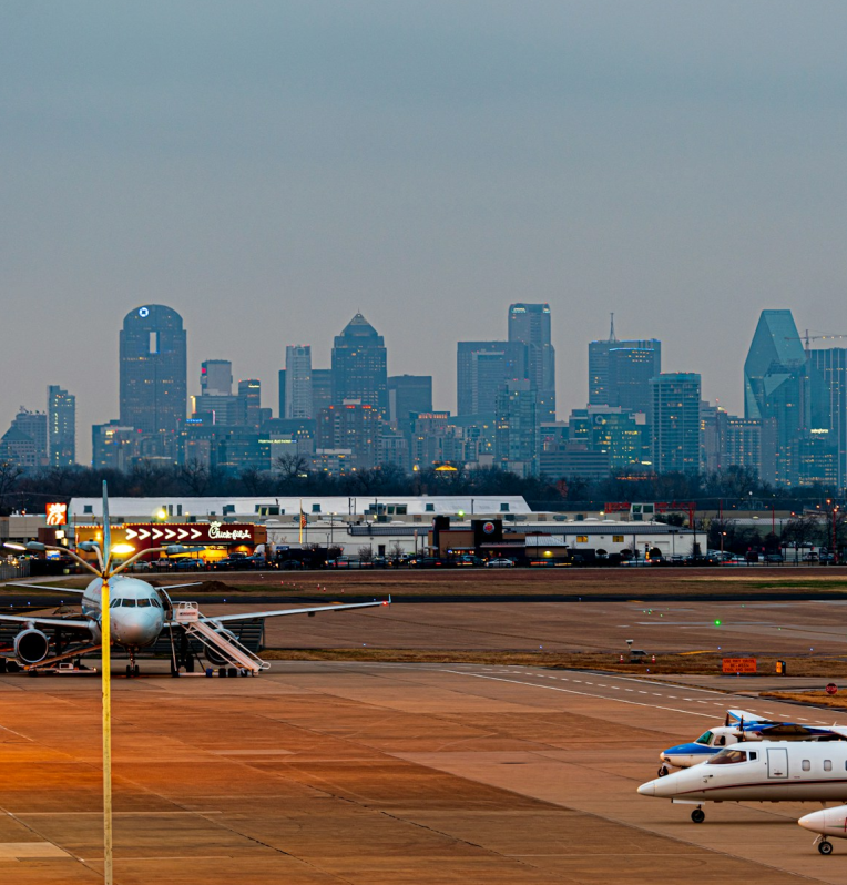 View of the Dallas skyline from an airport runway with commercial and private aircraft parked at Dallas Love Field.