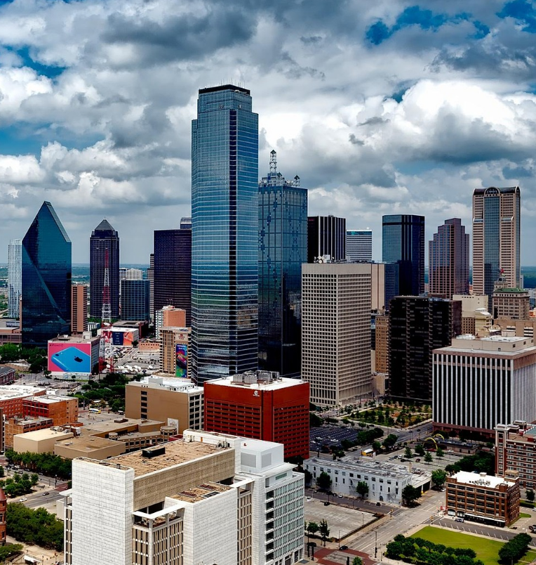 Aerial view of the downtown Dallas skyline featuring modern high-rise buildings and dramatic cloud formations over the city.