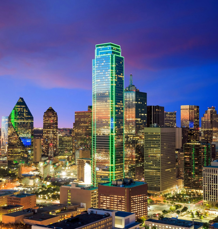 Nighttime skyline of downtown Dallas, Texas showcasing the illuminated Bank of America Plaza with green LED lights and surrounding high-rise buildings.