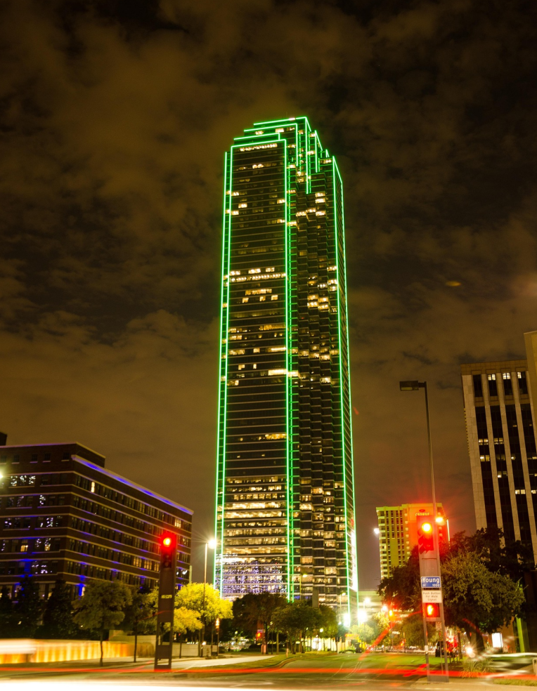 Hotels Near Dallas Fort Worth International Airport (DFW). Bank of America Plaza in downtown Dallas illuminated with bright green LED lights at night, showcasing the iconic Dallas skyline.