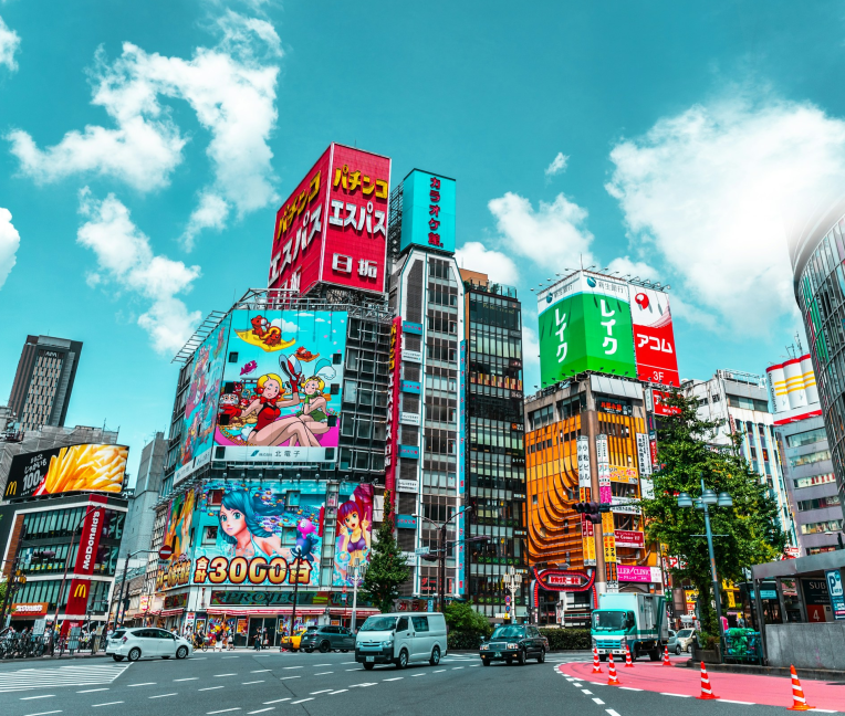 Colorful billboards and busy streets in Shibuya, Tokyo during the day with cars, pedestrians, and high-rise buildings.
