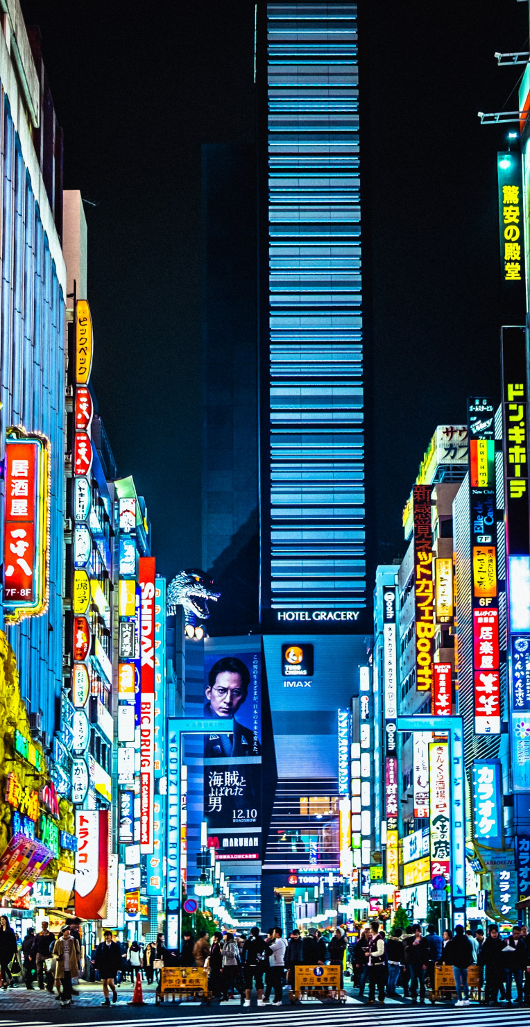 Where to Stay in Central Tokyo. Neon-lit Kabukicho street in Shinjuku, Tokyo at night with crowds, billboards, and Hotel Gracery visible.