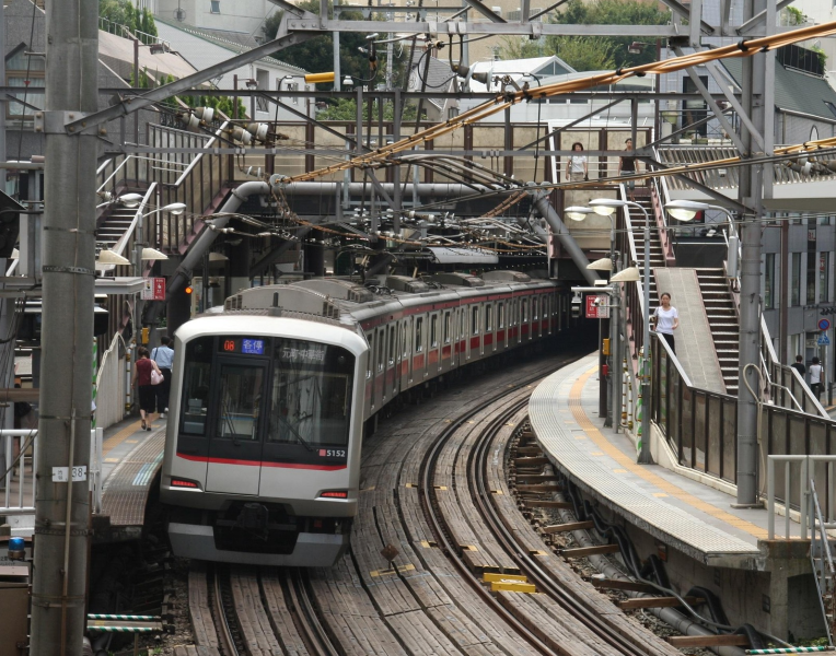Commuter train arriving at an urban railway station in Tokyo, Japan with tracks, platforms, and overhead lines.