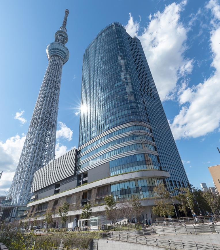 Tokyo Skytree towering beside modern buildings in Sumida, Tokyo on a clear daytime sky.