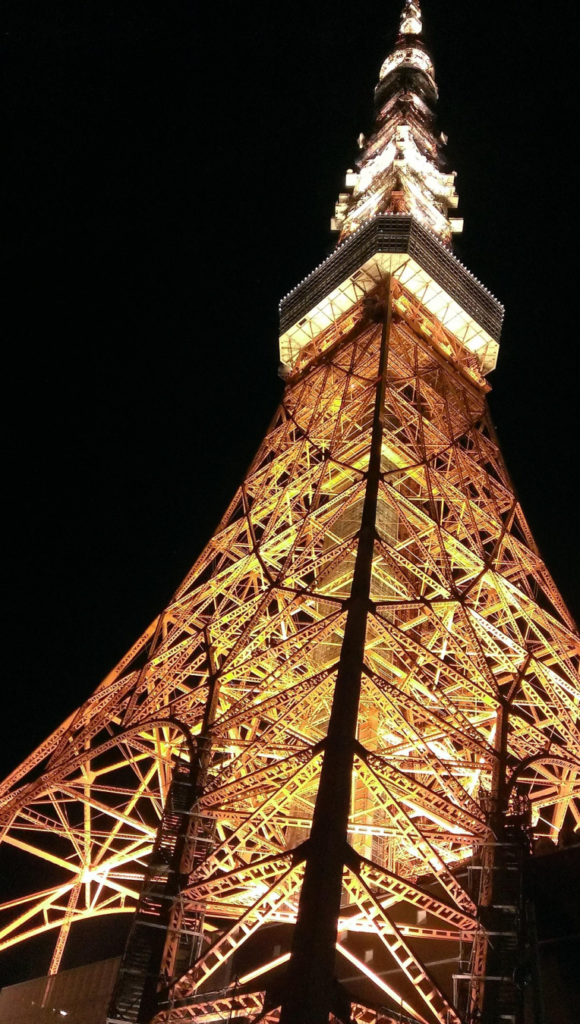 Tokyo Tower illuminated at night, viewed from below against a dark sky in Tokyo, Japan.