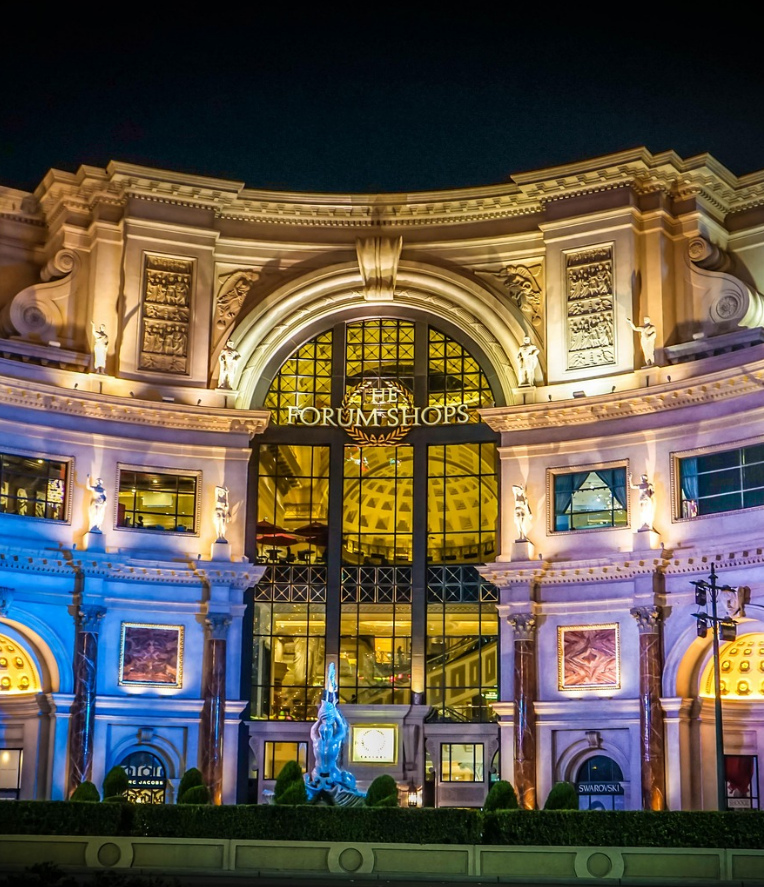 The Forum Shops at Caesars Palace in Las Vegas illuminated at night, featuring grand Roman-inspired architecture and elegant arched entrance on the Strip.