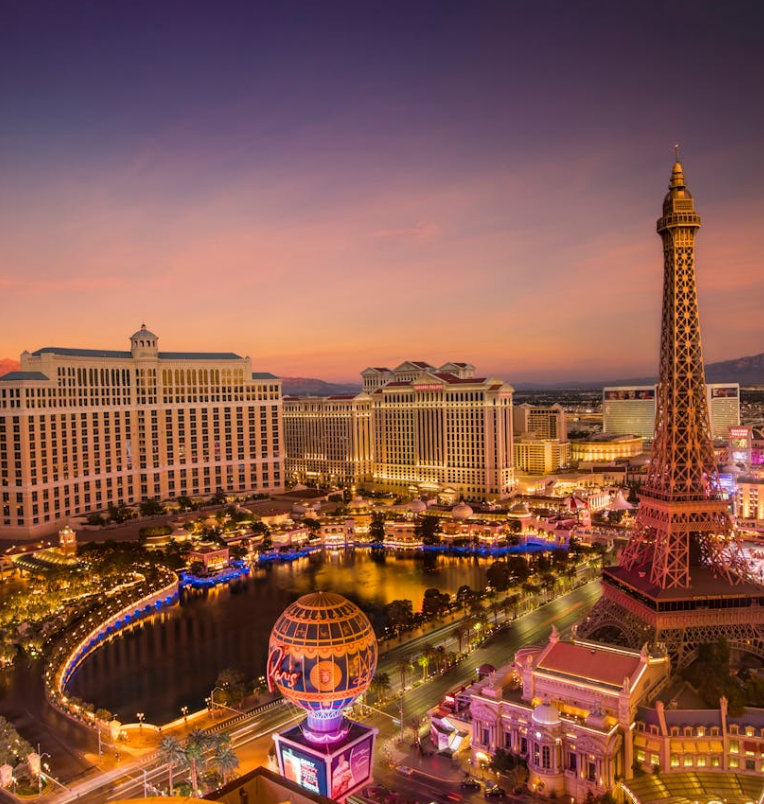 Las Vegas Strip at sunset featuring the Bellagio Hotel and fountains, Paris Las Vegas Eiffel Tower replica, and illuminated casino resorts under a colourful evening sky.