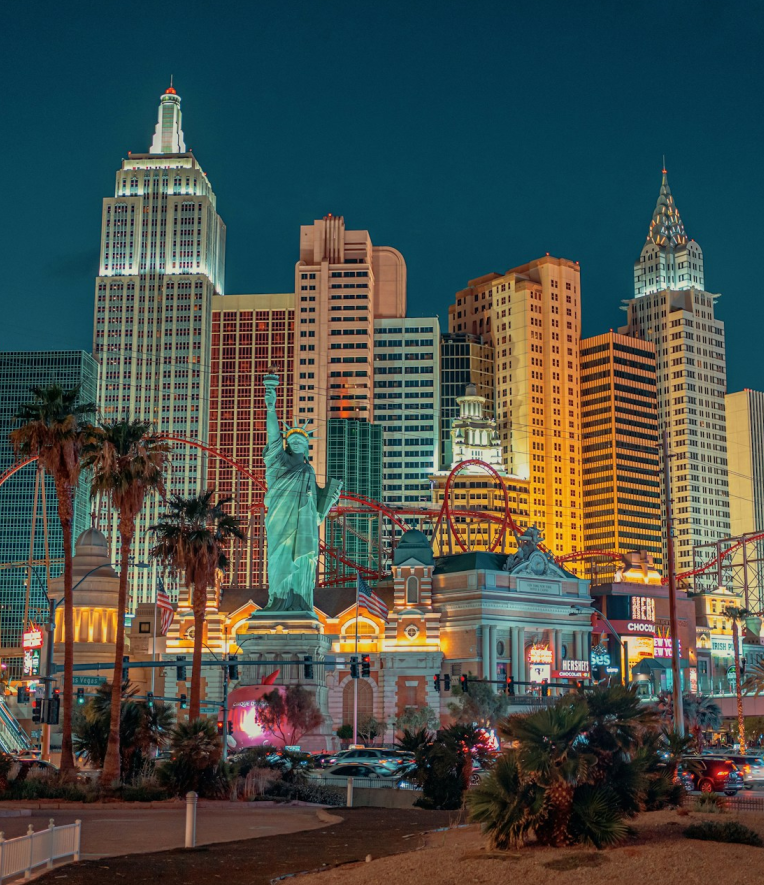 New York-New York Hotel and Casino in Las Vegas at night featuring the Statue of Liberty replica, illuminated skyline, and red roller coaster on the Strip.