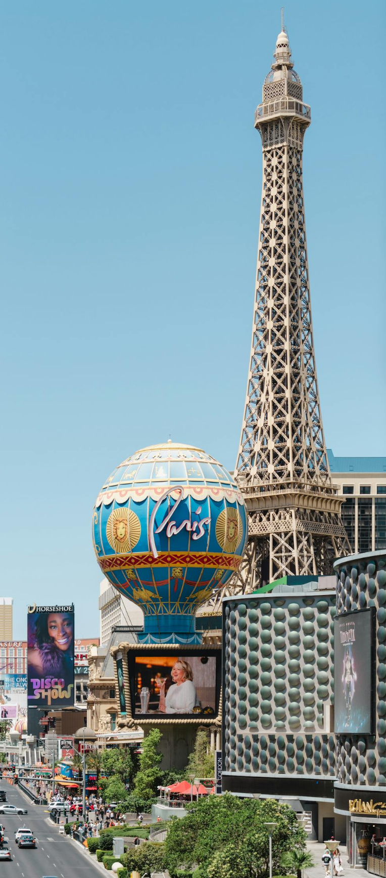 Where to Stay in Las Vegas. Paris Las Vegas Eiffel Tower replica and Paris balloon sign on the Las Vegas Strip, with casino buildings and busy boulevard under a clear blue sky.