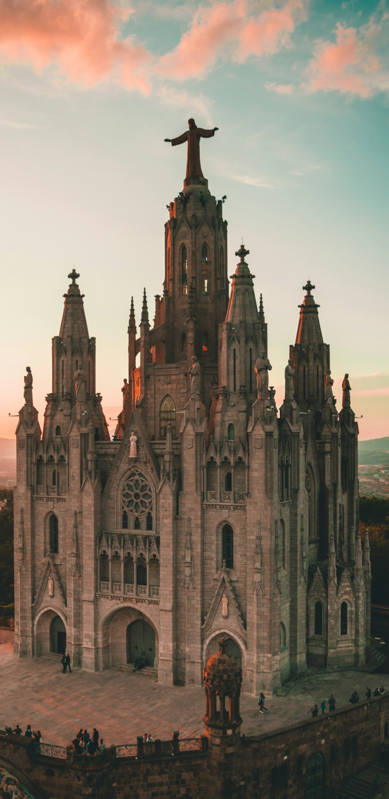 Where to Stay in Barcelona. Temple Expiatori del Sagrat Cor (Tibidabo Church) in Barcelona at sunset, featuring the neo-Gothic facade and statue of Jesus Christ overlooking the city.