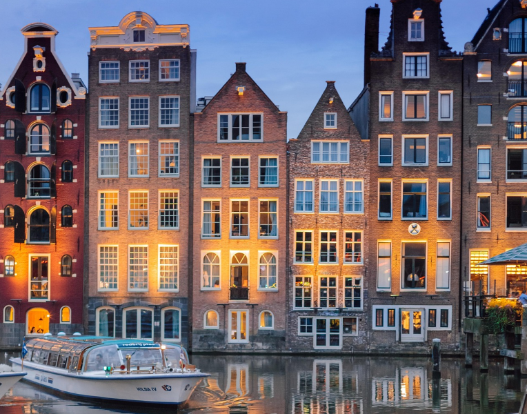 Traditional Amsterdam canal houses illuminated at dusk with a canal boat on the water in the Netherlands.
