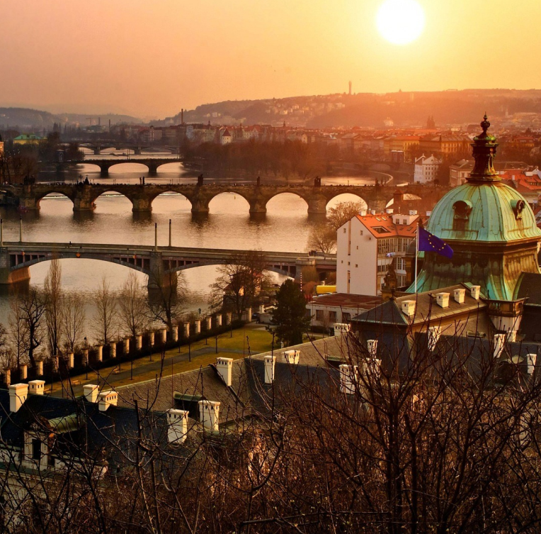 Sunset view of Prague with Charles Bridge over the Vltava River and historic rooftops glowing in golden light, Czech Republic.