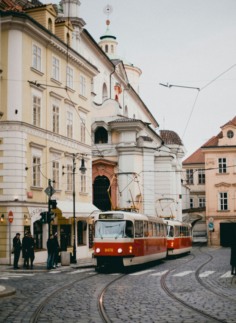 Historic red tram traveling through a cobblestone street in Prague Old Town with pastel buildings and tram tracks, Czech Republic.