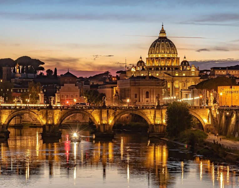 St Peter’s Basilica illuminated at sunset in Rome with bridge over the Tiber River and golden reflections on the water at dusk.