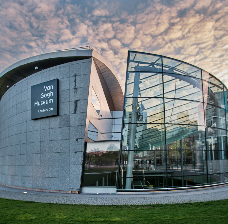 Van Gogh Museum in Amsterdam at Museumplein with modern curved architecture and glass facade under dramatic sky.