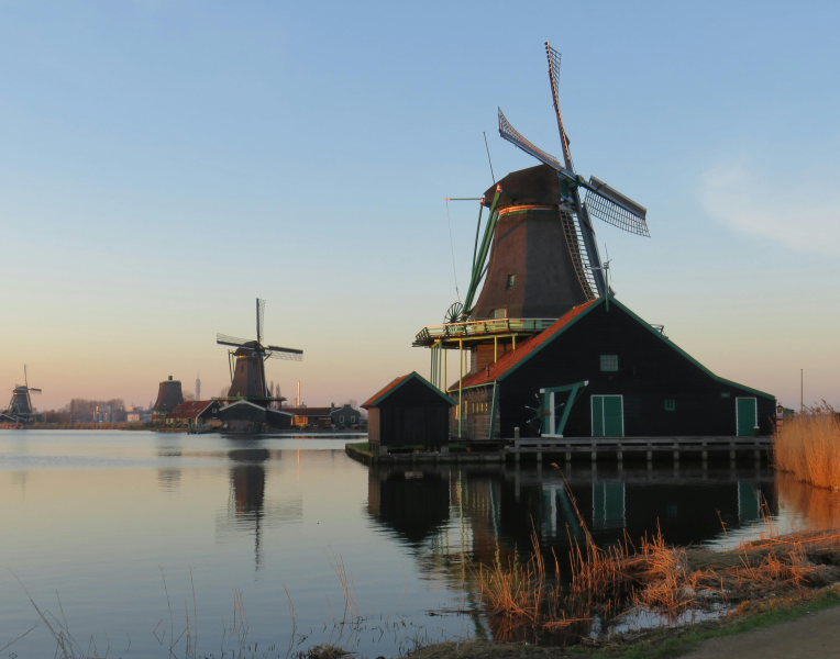 Traditional Dutch windmills at Zaanse Schans in the Netherlands reflected in calm water at sunset.