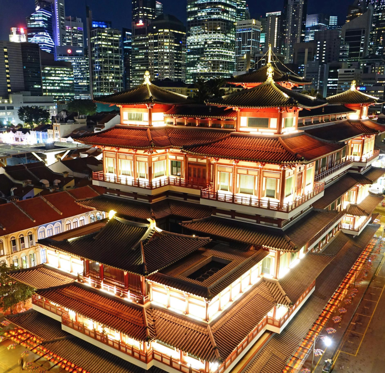 Illuminated Buddha Tooth Relic Temple in Singapore’s Chinatown at night, with modern CBD skyscrapers in the background.