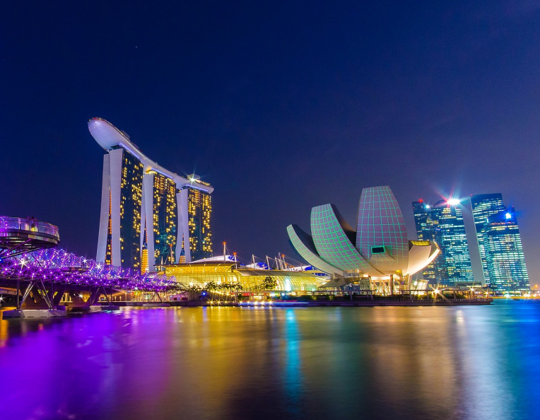 Singapore Marina Bay skyline at night with the illuminated Helix Bridge, Marina Bay Sands and ArtScience Museum reflected in the water.