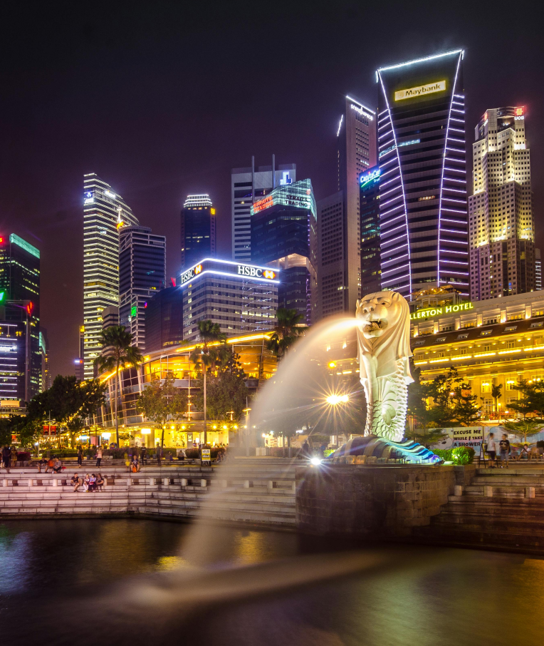 Singapore’s illuminated Merlion statue spraying water into Marina Bay at night, with the Central Business District skyline in the background.