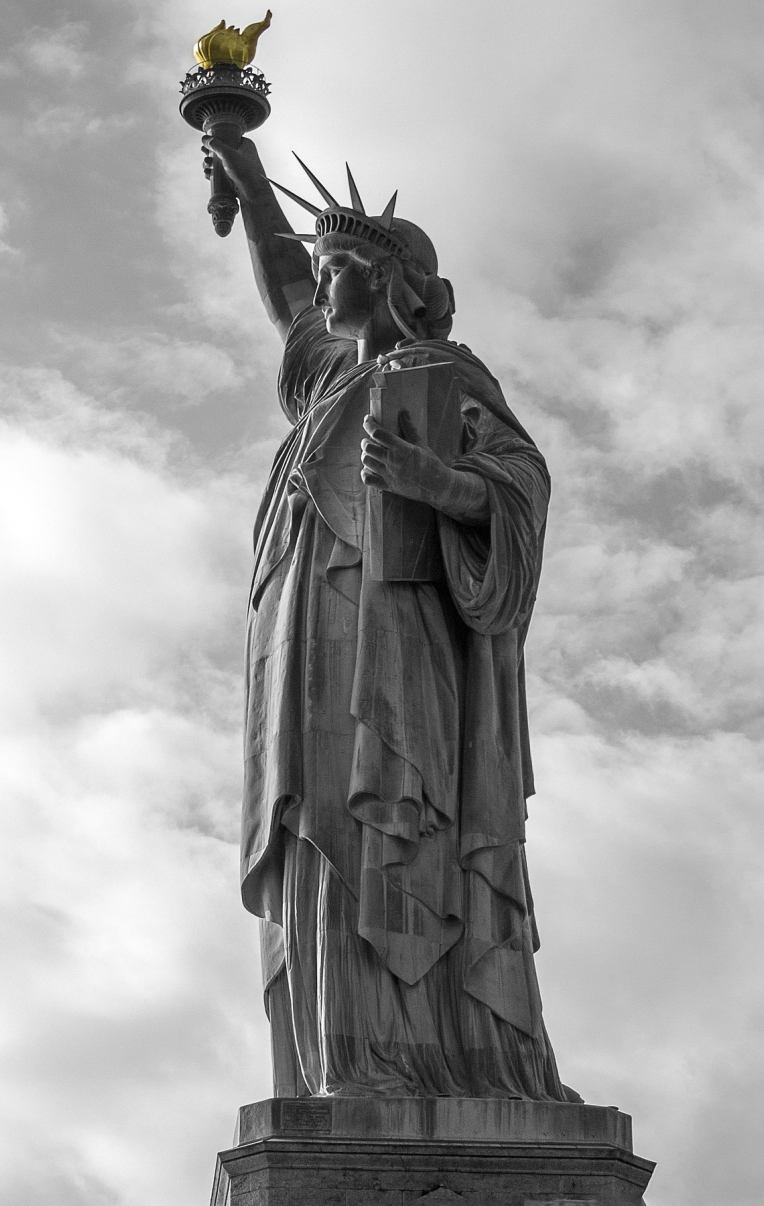 Close-up view of the Statue of Liberty in New York, with its golden torch highlighted against a cloudy sky.