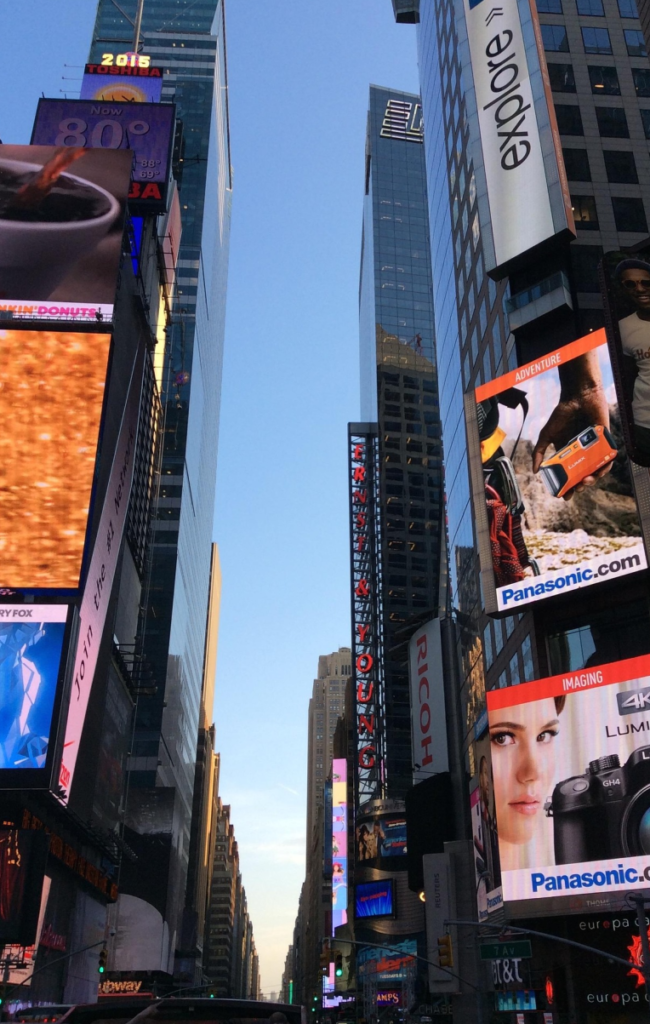 Times Square in Midtown Manhattan with tall buildings and large digital advertising billboards during the day.
